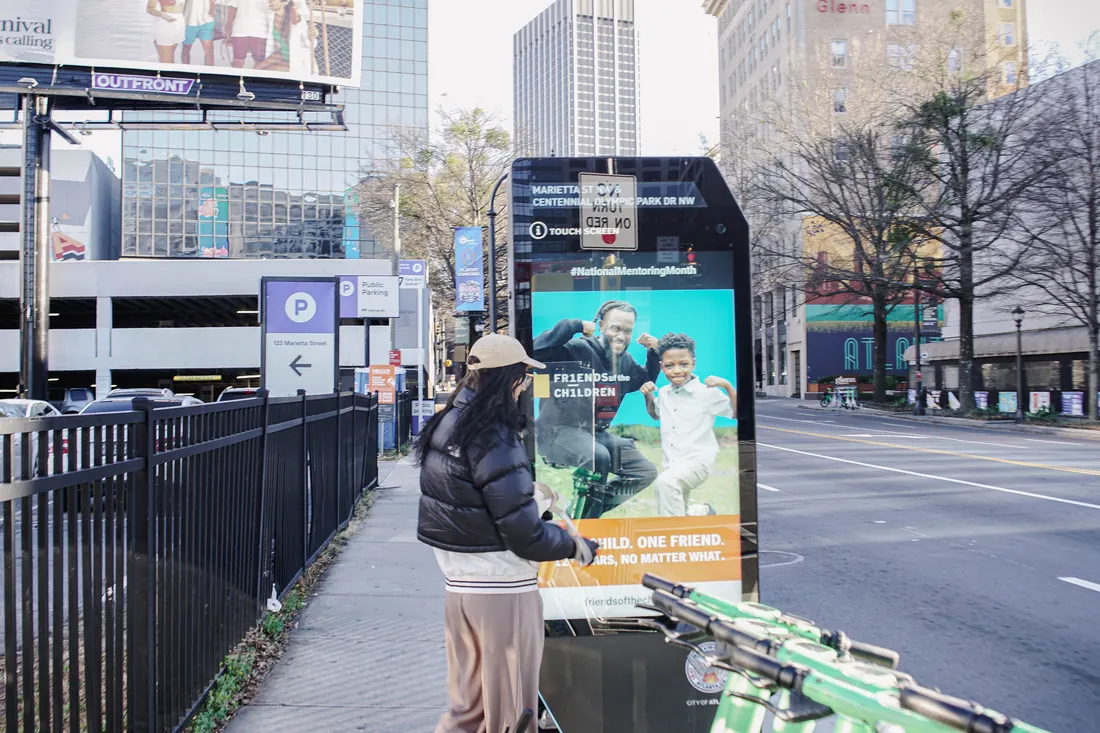 A pedestrian walking toward a downtown Atlanta kiosk beside a fenced sidewalk