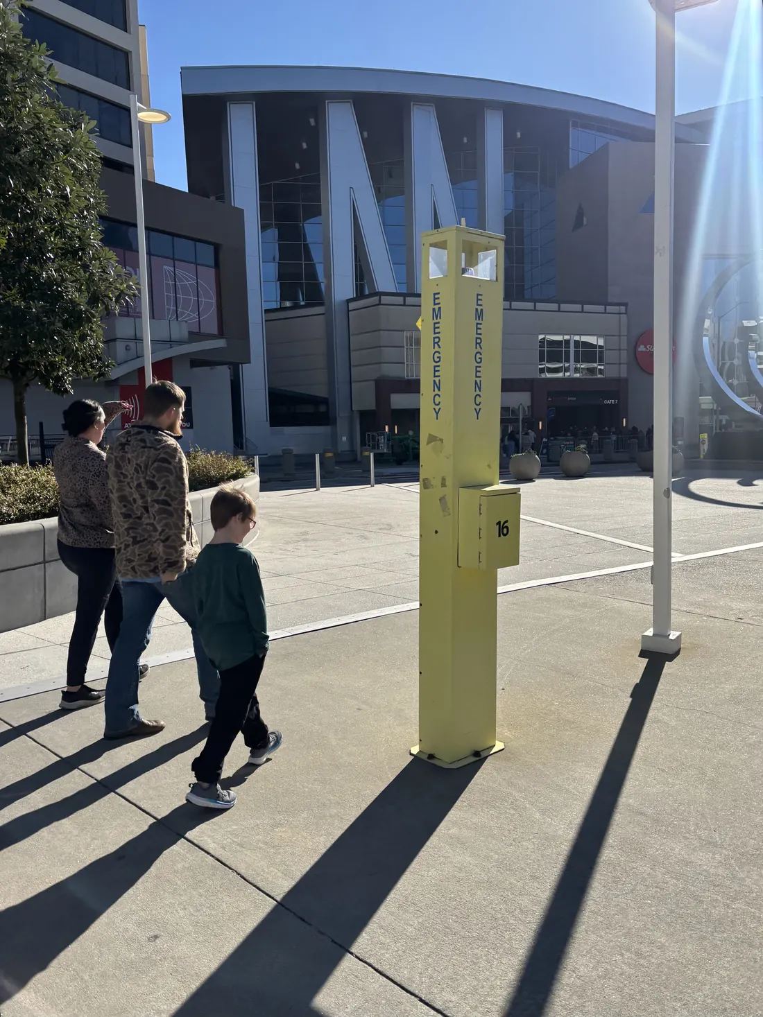 A yellow information post on a plaza with a large venue behind it